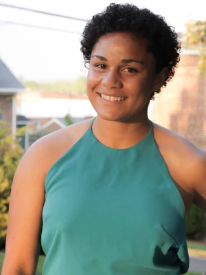 The photo shows a Black woman with short hair smiling at the camera. She is wearing a dark teal tank top.