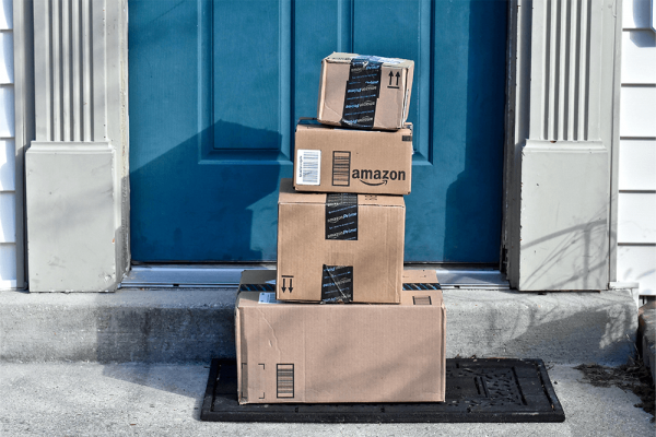 A stack of four Amazon boxes on a doormat outside a blue front door.