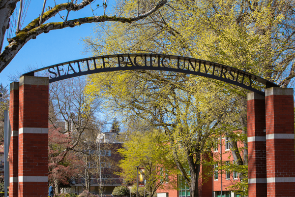 A metal archway says "Seattle Pacific University" in front of trees with yellow leaves. 