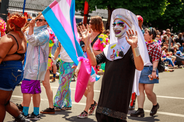 A person wearing heavy drag makeup and a black Catholic habit waves in a pride parade.