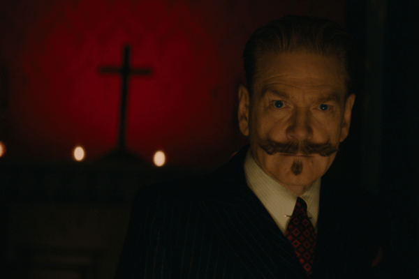 A man with a mustache looks on while a cross looms on a red background.