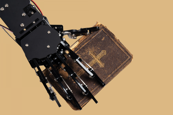 The picture shows a robotic hand holding a Bible on a tan/gold background 