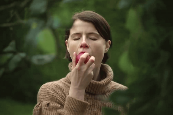 A white woman who has closed eyes bites into an apple