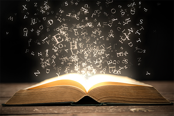 A glowing book on a table with letters bursting out of it and floating in the air.