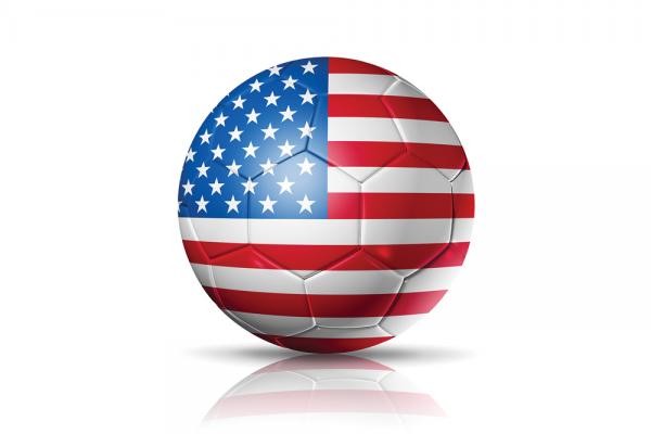 An illustration of a soccer ball with an American flag all over its surface. It's on the ground of a completely white background.