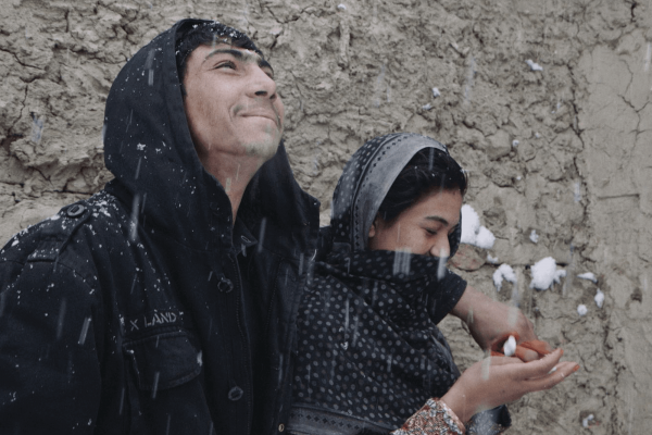 A husband and wife stand close to each other and enjoy falling snow