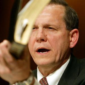 Justice Roy Moore holds a Bible while testifying in a hearing. Via Getty Images.