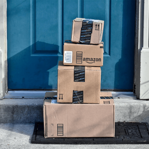 A stack of four Amazon boxes on a doormat outside a blue front door.