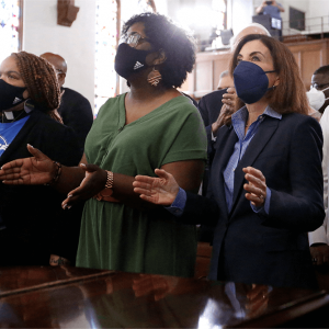 A diverse crowd of people stand in a church wearing masks during a vigil.