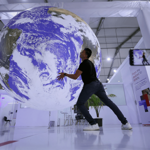 An attendee poses for a picture near a large model earth inside a large room.