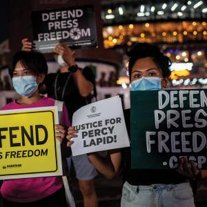 A group of Filipinos stand together, wearing masks and carrying signs that hold variations on the phrase "Defend Press Freedom"