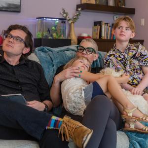 A family photo of trans Christian Sid High's family sitting on a couch in their living room as they look off to the side. Sid's dad sits on the left; Sid's mom sits in the center with his younger sister in her lap; Sid sits on the right.