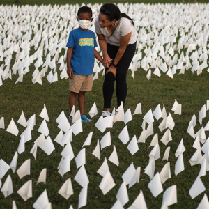 A Black woman leans to speak to a masked Black child amid a sea of small, white flags