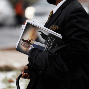 A person wearing a black suit carries a paper program with a photo and name of Tyre Nichols.