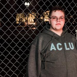 Gavin Grimm, a 17-year-old transgender boy, stands in front of a chainlink fence.