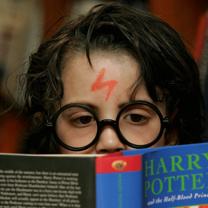 A young child reading 'Harry Potter and the half blood prince' dressed up as Harry Potter