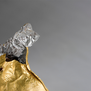 A Chocolate Easter bunny, wrapped in shiny golden and silver aluminum foil, partially nibbled away, foil ripped open at the top