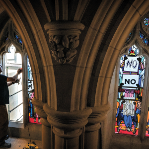 The photo shows a man replacing stained glass windows at the Washington National Cathedral, the new windows have protest art on them. 