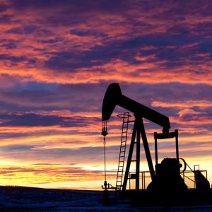 A pumpjack retrieves oil from the group against a sunset background