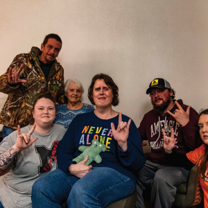 The image shows six people holding up the sign language for "I love you" 