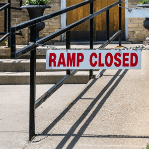 A red and white sign stating 'ramp closed,' is chained to black iron handrails in front of church ramp entrance.