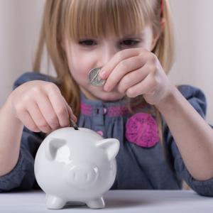 A young girl puts money in a piggy bank. Image courtesy Sofya Apkalikova/shutter