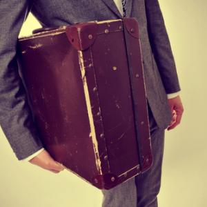 A young man carries an old suitcase. Image courtesy nito/shutterstock.com.