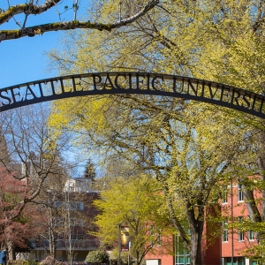 A metal archway says "Seattle Pacific University" in front of trees with yellow leaves. 