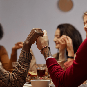 A multiracial group of people hold hands in prayer at Thanksgiving dinner. 