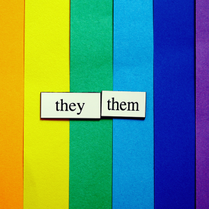 The words they and them on a background of rainbow colored paper.