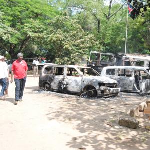 A man walks past burnt cars destroyed during a terror attack in Lamu country, Ju