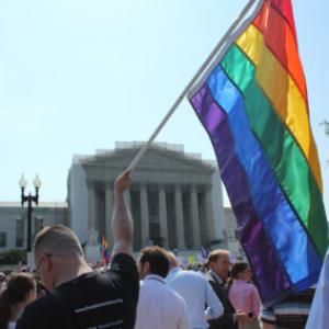 A man holds a gay pride flag in front of the Supreme Court. Photo via Adelle M. 