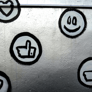 Social media icons of hearts, like buttons, and smiling emojis are spray painted on a silver wall.