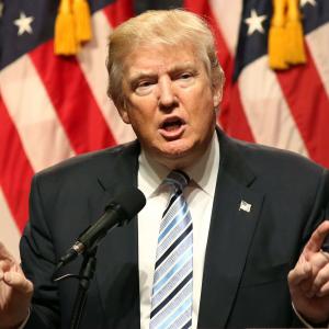 Trump speaks to a gathered audience before an American flag backdrop.