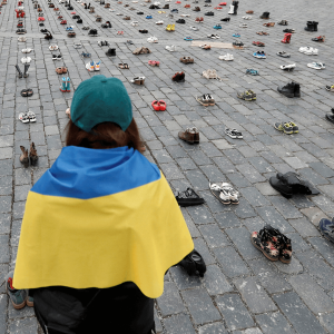 A woman wrapped in a Ukrainian flag looks at pairs of shoes arranged in rows.
