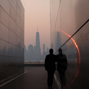 A man stands in the Empty Sky 911 Memorial in Jersey City, New Jersey looking towards the One World Trade Center tower in lower Manhattan in New York City shortly after sunrise as haze and smoke hangs over the Manhattan skyline