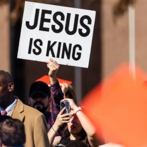 A man holds a sign reading "Jesus is king" in a crowd of people.