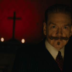 A man with a mustache looks on while a cross looms on a red background.