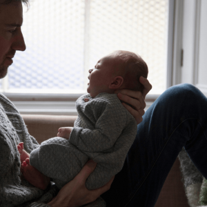 A man holds a crying baby in front of a window.