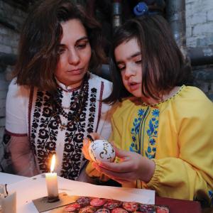A Ukrainian woman and girl are sitting together as they paint an Easter egg.