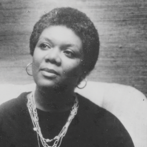 A black-and-white photo of poet Lucille Clifton, sitting in a chair wearing black robes and several layered necklaces.