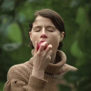 A white woman who has closed eyes bites into an apple