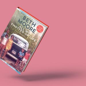 An image of Beth Moore's memoir 'All My Knotted-Up Life' against a pink backdrop. The cover shows her as a child posing with her family as they stand behind and to both sides of an old navy and white van outside near a forest.