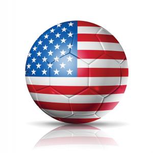 An illustration of a soccer ball with an American flag all over its surface. It's on the ground of a completely white background.