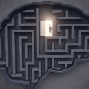 A birds-eye view of a textured gray background overlaid with a maze in the shape of a brain. In the top third of the brain, a figure silhouetted by golden light walks through an open door.