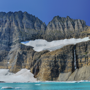 The picture shows a melting glacier and the pool of meltwater that has formed beneath it. The remaining snow is on a mountain. 