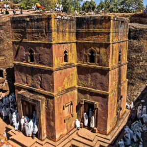 the photo is a image of a red church carved out of rock. The church has pilgrims surrounding it, all of them wearing white