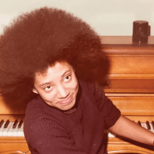 A young Nikky Finney sits at a piano with her father in 1972.