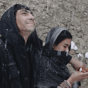 A husband and wife stand close to each other and enjoy falling snow