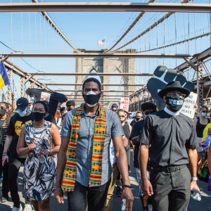 Jumaane Williams walks in front of a group of masked Black people crossing the Brooklyn Bridge
